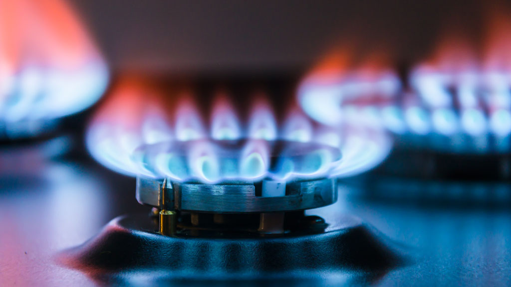 Chef cuisinier travaillant devant un piano de cuisson professionnel à gaz avec flammes bleues visibles